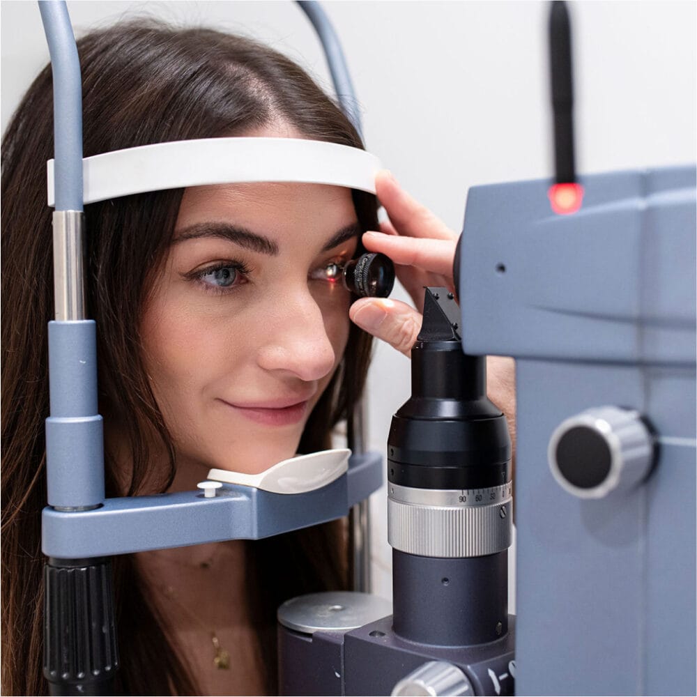 Patient having an eye exam with an ophthalmologist using a slit-lamp microscope, resting her chin on the exam support during evaluation.
